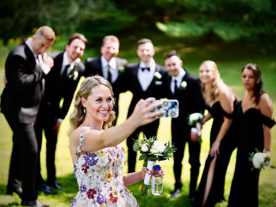 Braut macht ein Selfie mit der ganzen Hochzeitsgesellschaft im Hintergrund